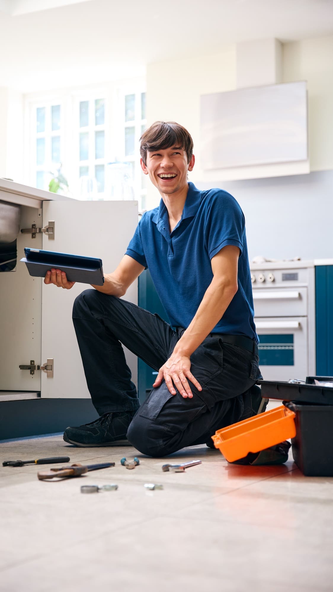 Portrait Of Male Plumber With Digital Tablet Fixing Waste Disposal Unit In Domestic Kitchen Sink